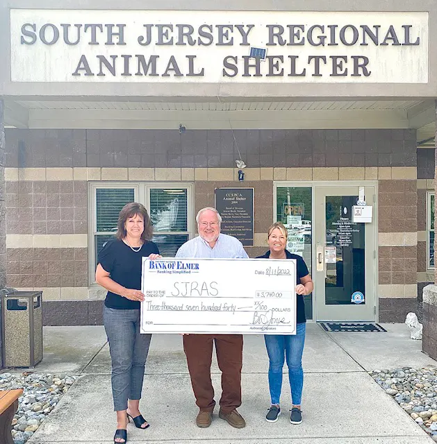 Man holding up large check with two women in front of animal shelter
