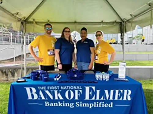 Four adults standing under pop-up tent behind Bank of Elmer bannered table