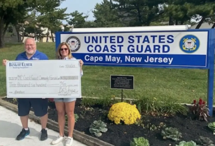 Man and woman holding up giant check in front of Coast Guard sign outdoors