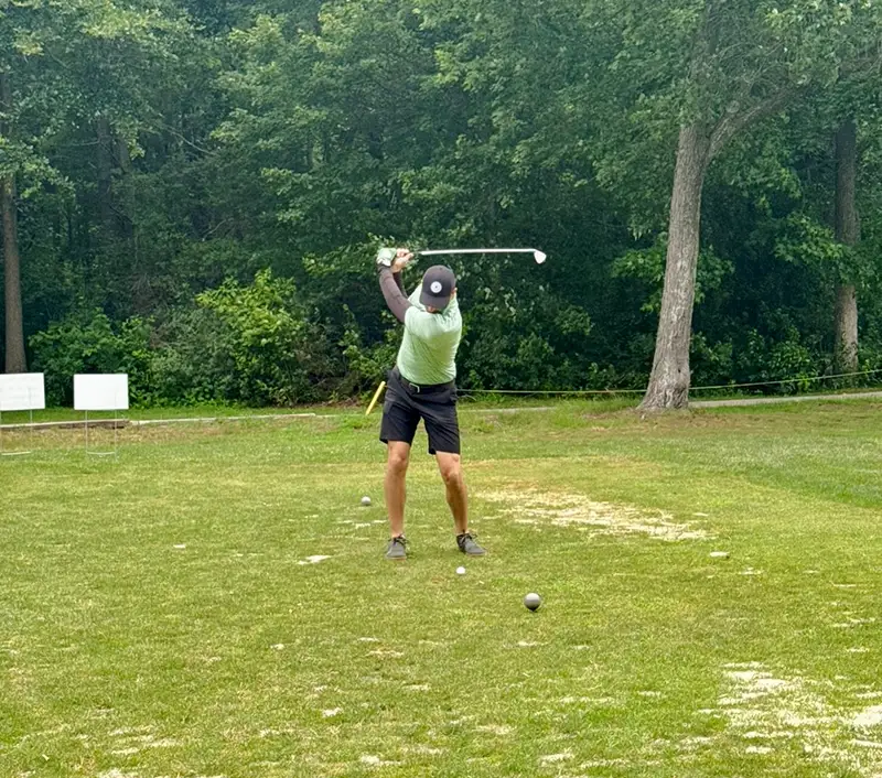 Man in light green and black athletic wear reeling back to hit golfball.