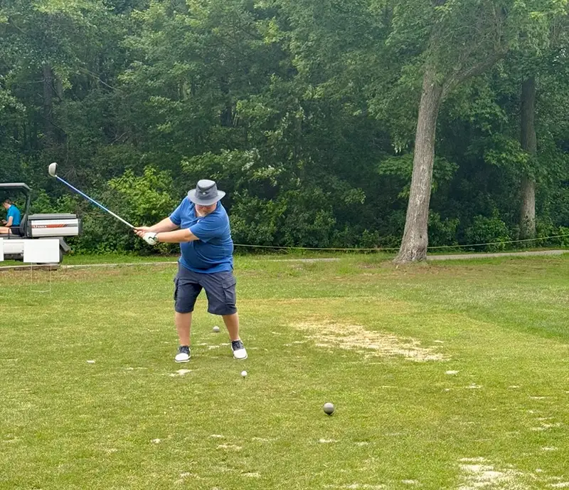 Man in blue outdoor wear swinging golf club to hit golf ball.