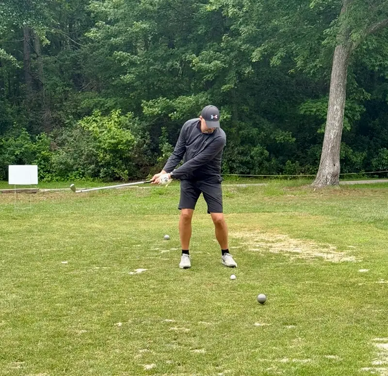 Man in dark gray sports gear preparing to hit a golf ball.