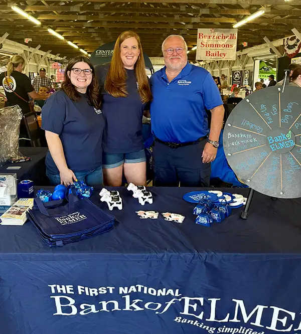 Two Elmer Bank employees and Elmer Bank President pose behind the Elmer Bank Fair table.