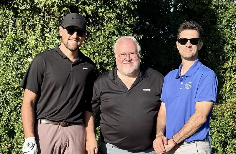Three men posing outside with golfclubs.