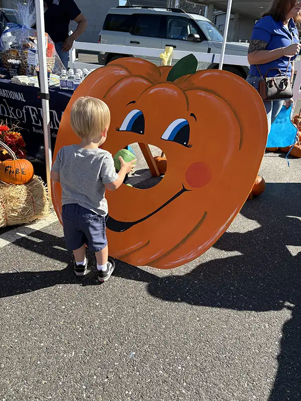 Young child next to painted pumpkin board with hole.