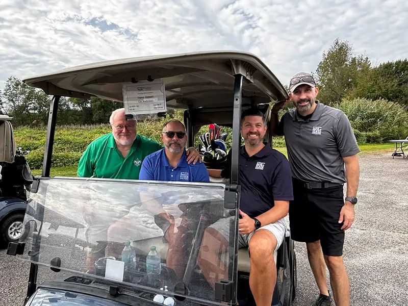 Four men are posing for picture on a golf cart.