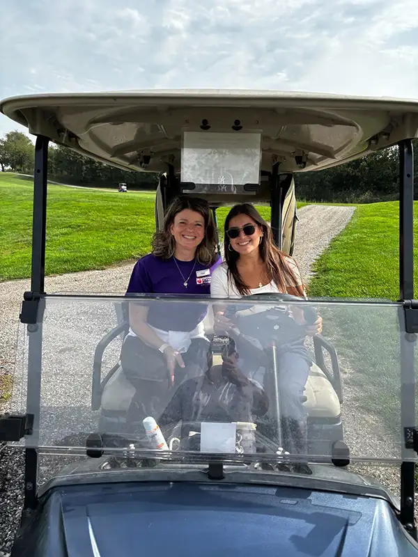 Two women posing for picture in a golf cart.