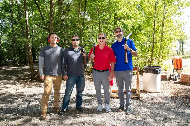 Four men posing outside with clay shooting gear.