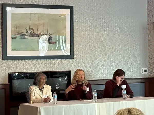Three women at a table. One speaking into a microphone.